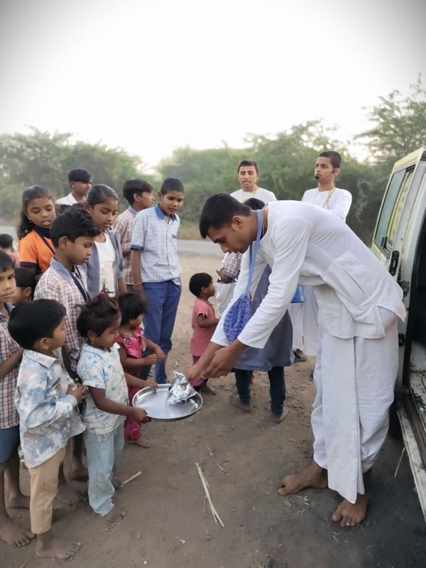 Devotees dancing in harinam sankirtan with village children under a tree at dusk