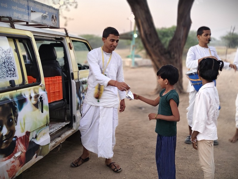 A devotee distributing prasadam to a child beside the temple food-distribution van